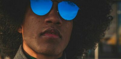 En mann med afro og solbriller stirrer ut i luften. Foto