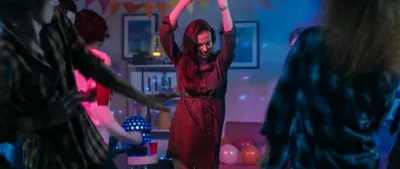 En dame står å danser i et rom med mange mennesker. Foto
