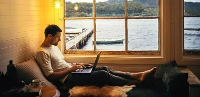En mann sitter på en sommerhytte og jobber på en laptop. Foto