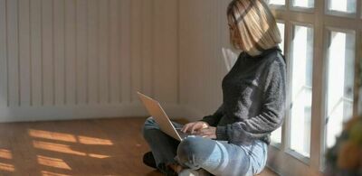 En dame sitter på gulvet og jobber på en laptop. Foto