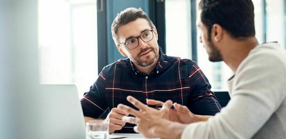 To menn sitter og diskuterer ved et bord. Foto