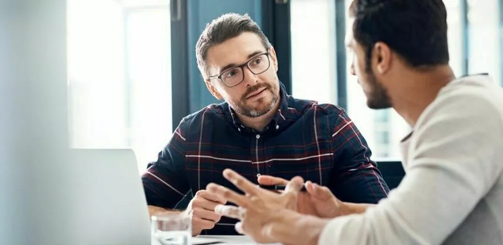 To menn sitter og diskuterer ved et bord. Foto