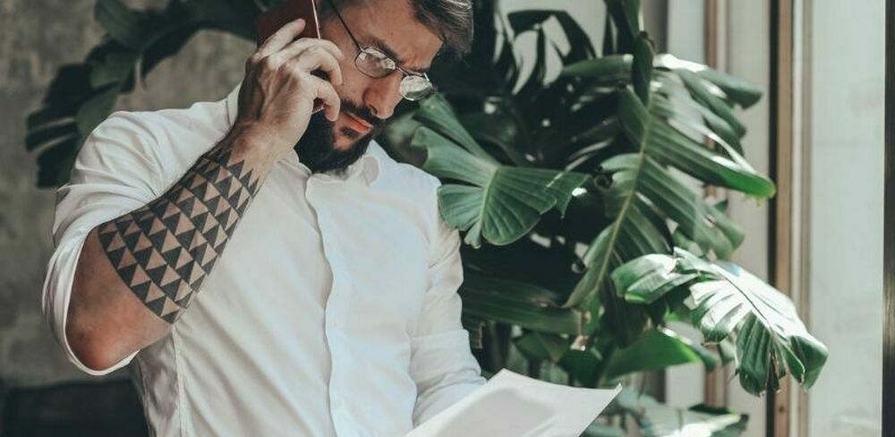 En mann snakker i telefonen og ser ned på et ark. Foto